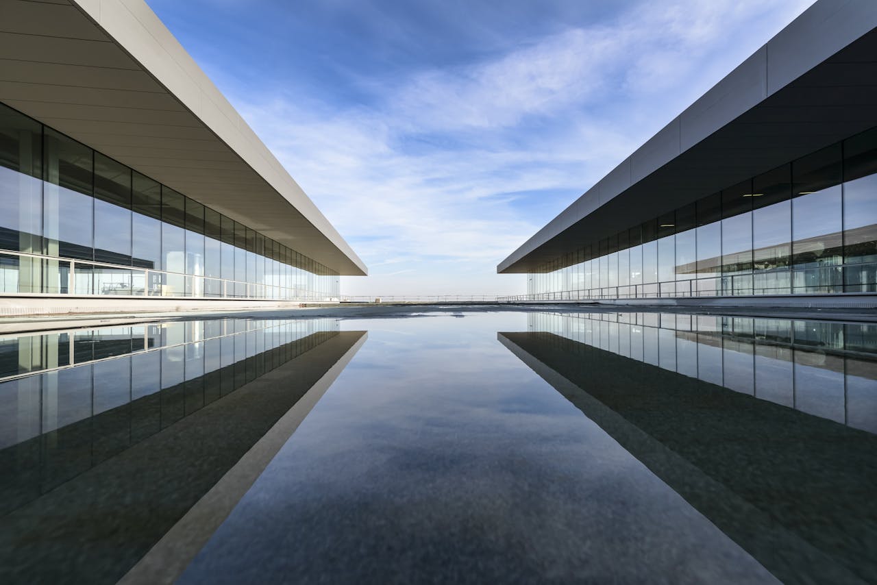 hero-services Futuristic glass building mirrored on a still water surface with a cloudy sky.